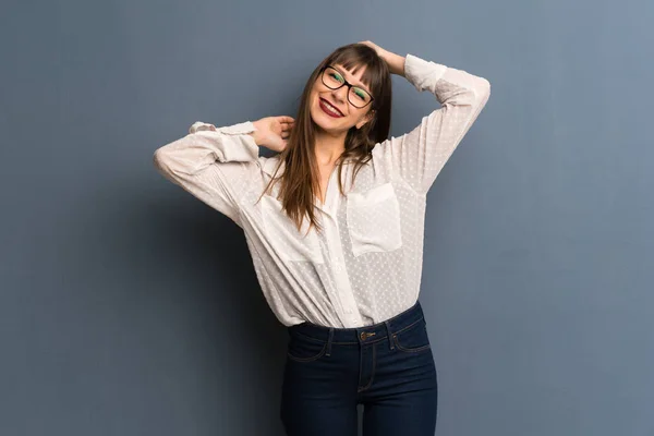 Woman with glasses over blue wall smiling