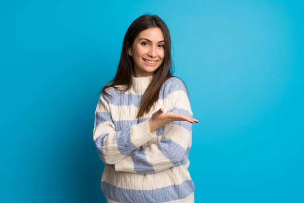 Young woman over blue wall presenting an idea while looking smiling towards