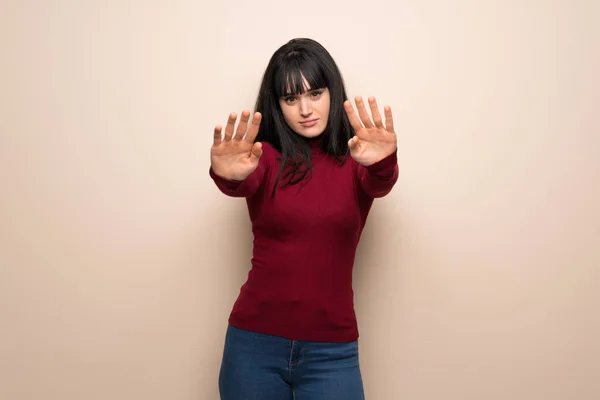 Young woman with red turtleneck making stop gesture for disappointed with an opinion