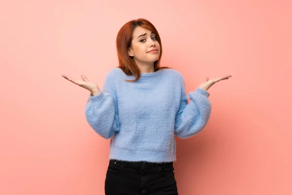 Young redhead woman over pink background making unimportant gesture while lifting the shoulders