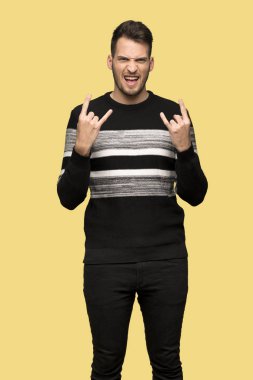 Yakışıklı adam yapma rock jest sarı arka plan üzerinde