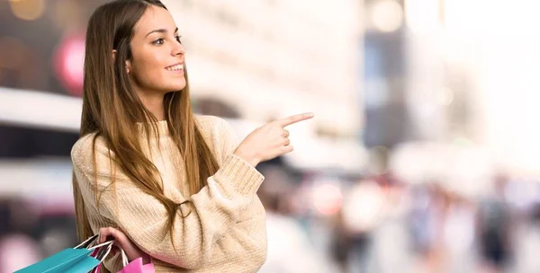 Chica Joven Con Bolsas Compras Apuntando Con Dedo Hacia Lado — Foto de Stock