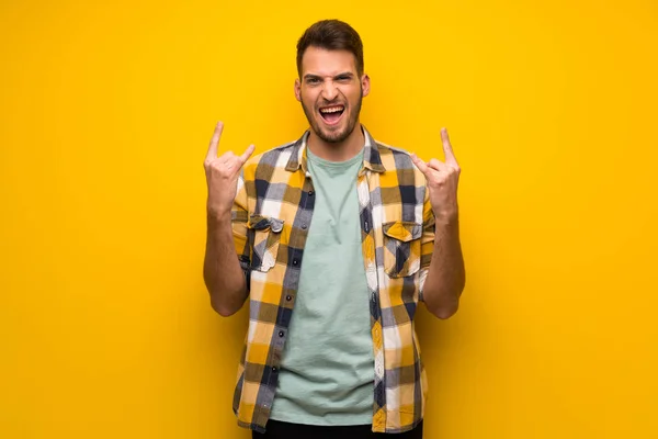 Handsome man over yellow wall making rock gesture