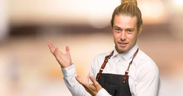 Barber man in an apron extending hands to the side for inviting to come in a barber shop