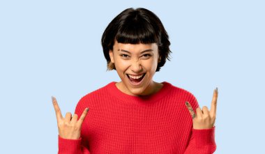 Kısa saçlı kız kırmızı kazaklı rock jest yapma ile mavi arka plan izole