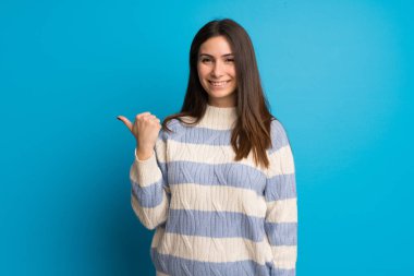 Mavi duvar tarafına işaret eden bir ürün sunmak için genç kadın