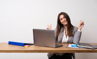 İş kadını gülümseyen ve her iki el ile zafer işaret gösteren bir ofiste