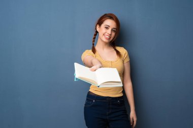 Bir kitap ve birine vererek mavi arka plan genç Kızıl saçlı kadın