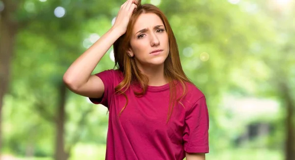 Young redhead girl with an expression of frustration and not understanding in the park