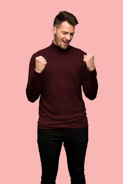 ピンクの背景の上の勝利を祝って タートルネックのセーターを持つ男 — ストック写真