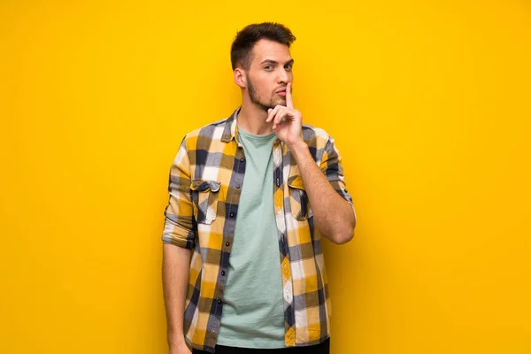 Handsome man over yellow wall showing a sign of silence gesture putting finger in mouth