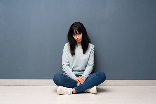 Woman sitting on the floor with sad and depressed expression
