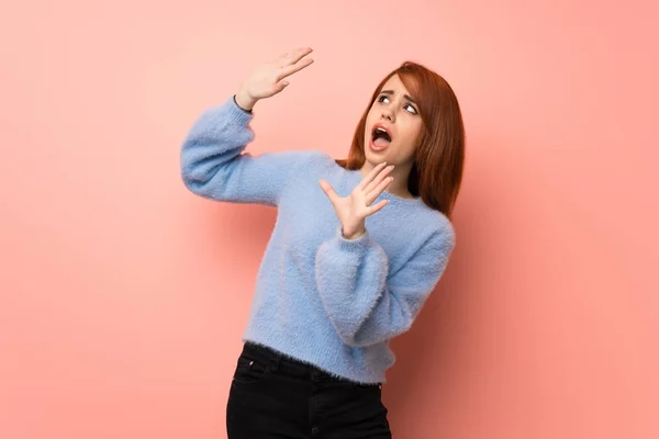 Young redhead woman over pink background is a little bit nervous and scared