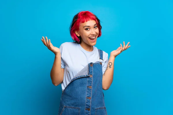 Young woman with pink hair over blue wall smiling a lot