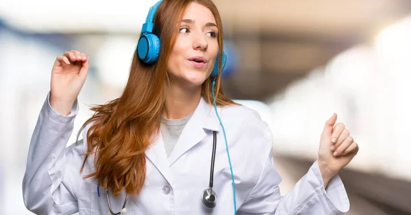 Redhead doctor woman listening to music with headphones and dancing in the hospital