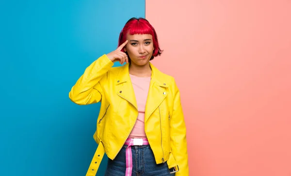 Young woman with yellow jacket making the gesture of madness putting finger on the head