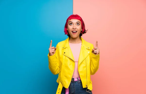 Young woman with yellow jacket surprised and pointing up