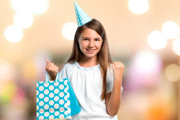 Menina em uma festa de aniversário segurando um saco de presente celebrando uma vitória em fundo desfocado — Fotografia de Stock