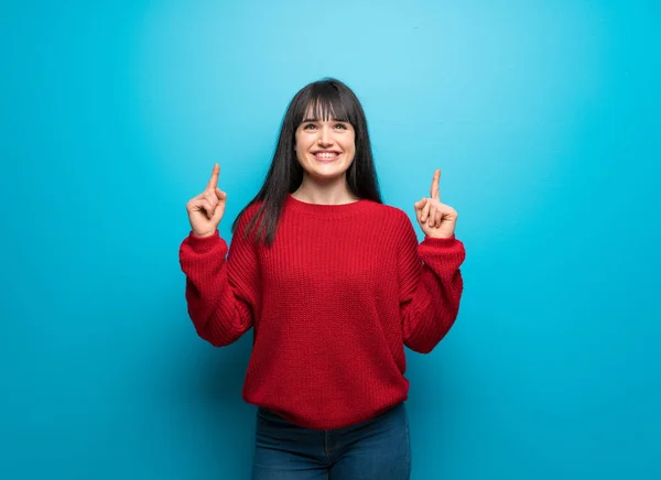 Woman with red sweater over blue wall pointing with the index finger a great idea