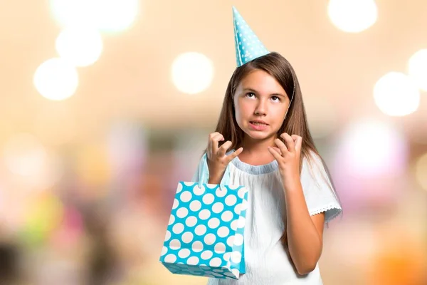 Ragazzina ad una festa di compleanno con una borsa regalo infastidito arrabbiato in gesto furioso su sfondo sfocato — Foto Stock