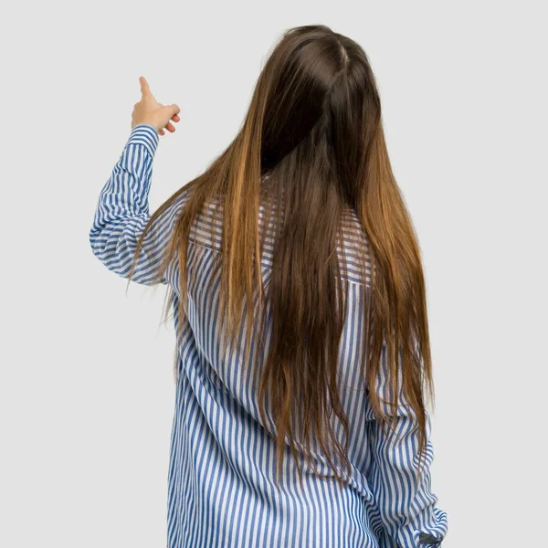 年轻的女孩与条纹衬衫指向后面与食指在孤立的灰色背景 — 图库照片