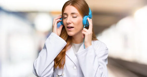 Redhead doctor woman listening to music with headphones in the hospital