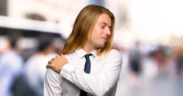 Blond businessman with long hair suffering from pain in shoulder for having made an effort at outdoors