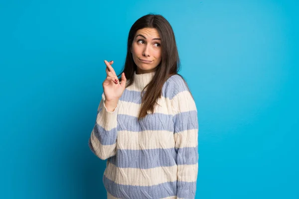 Young woman over blue wall with fingers crossing and wishing the best