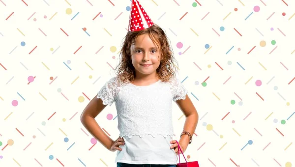Dziewczynka na przyjęcie urodzinowe, trzymając torba prezent pozowanie z ramion na biodra na kolorowe tło — Zdjęcie stockowe