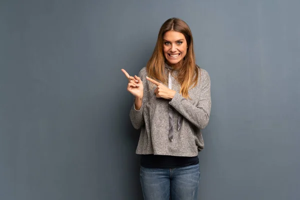 Mujer Rubia Sobre Fondo Gris Asustado Señalando Lado —  Fotos de Stock