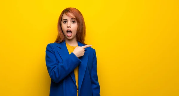 Young redhead woman with trench coat surprised and pointing side