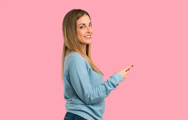 青いシャツ分離ピンク背景に 携帯電話でメッセージを送信すると金髪女性 — ストック写真