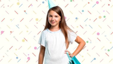 Küçük kız kalça renkli arka plan üzerinde silah ile poz bir hediye çanta tutan bir doğum günü partisinde