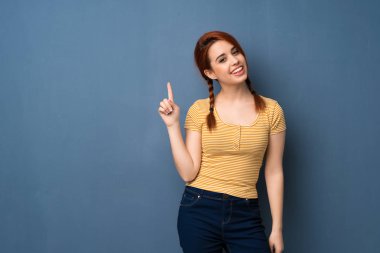 Gösteren ve en iyi iz içinde parmak kaldırma mavi arka plan genç Kızıl saçlı kadın