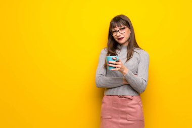 Bir fincan sıcak kahve tutan sarı duvarın üzerinden gözlüklü kadın