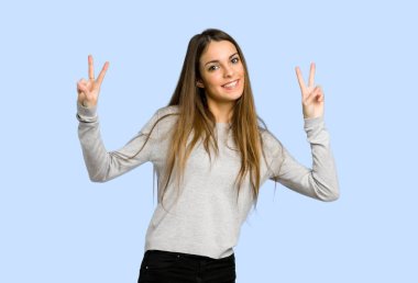 gülümseyen ve zafer işareti her iki el ile mavi arka plan üzerinde gösterilen genç kız