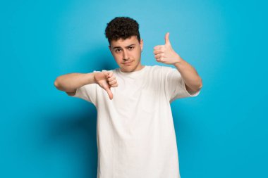 Mavi arka plan iyi-kötü işaret yapma genç adam. Arasında kararsız Evet ya da değil