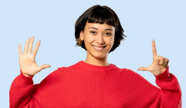 Kısa saçlı kız kırmızı kazaklı yedi ile izole mavi zemin üzerine parmak sayma