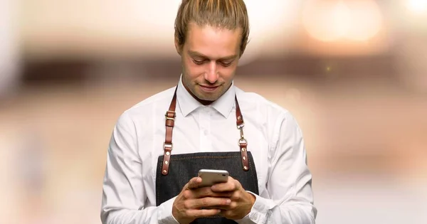 Barber man in an apron sending a message with the mobile in a barber shop