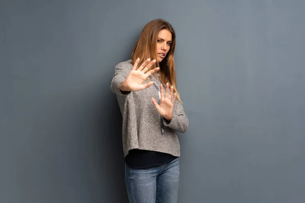 Blonde woman over grey background nervous and scared stretching hands to the front