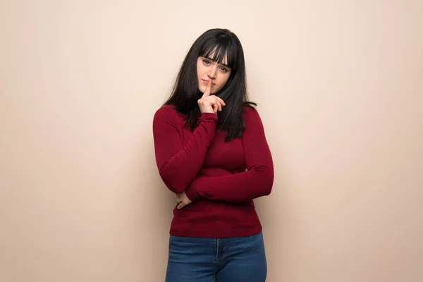 Young woman with red turtleneck showing a sign of silence gesture putting finger in mouth