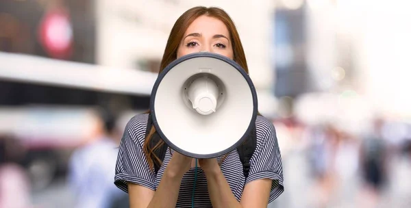 Redhead student woman shouting through a megaphone to announce something in the city