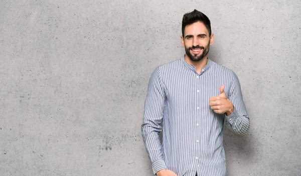 Elegant man with shirt giving a thumbs up gesture with both hands and smiling over textured wall