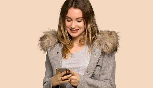 Dospívající Dívka Kabátem Odesláním Zprávy Mobilním Telefonem Izolované Žluté Pozadí — Stock fotografie