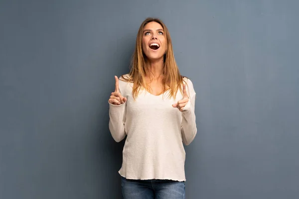 Mujer Rubia Sobre Fondo Gris Sorprendida Señalando Hacia Arriba —  Fotos de Stock