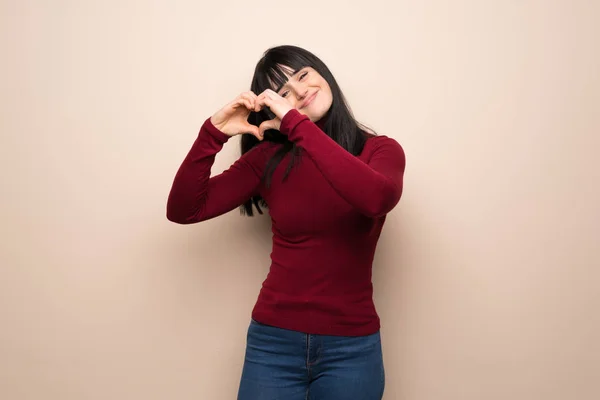 Young woman with red turtleneck making heart symbol by hands