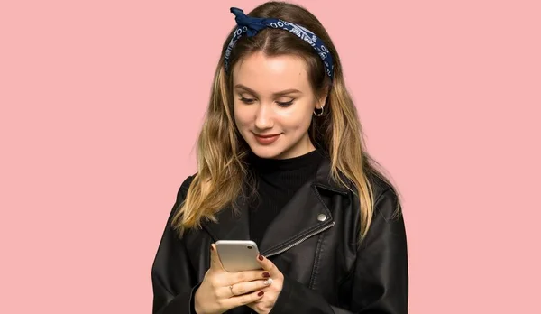 レザー ジャケットの分離ピンク背景に 携帯電話でメッセージを送信するとティーンエイ ジャーの女の子 — ストック写真