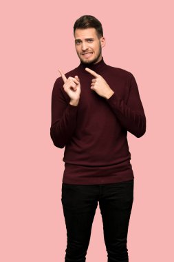 Adam korkmuş ve pembe arka plan üzerinde tarafına işaret balıkçı yaka kazak