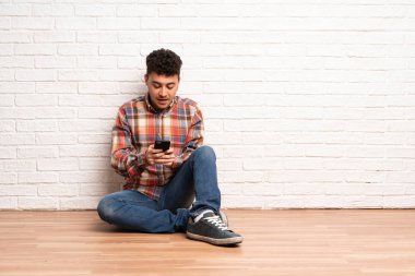 Yerde oturan genç adam cep telefonuyla mesaj yolluyor.