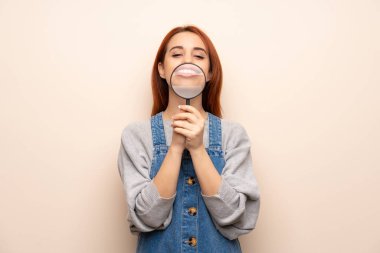 Büyüteç alarak ve o dişlerini gösteren izole arka plan genç Kızıl saçlı kadın